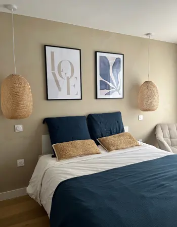 chambres avec mur à la chaux beige, décoration simple avec des suspension en osier de chaque coté du lit et des cadres au mur dans les teintes du mur et de la parure de draps (bleu)